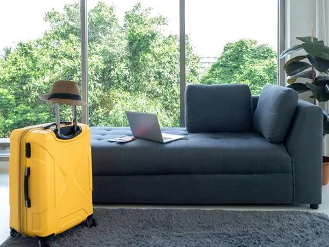 Empty grey cozy fabric sofa seat with laptop computer and yellow suitcase wit Stock Photos