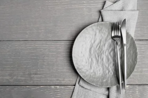 Empty grey plate, fork, knife on grey napkin on grey wooden table. Mock up... Stock Photos