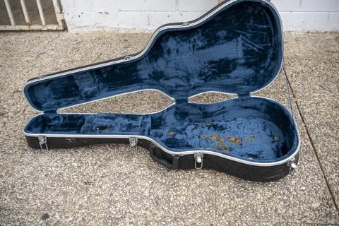 Empty guitar case placed on floor near wall with fence Stock Photos
