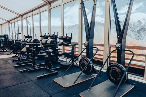 Empty gym with ski ergometers and weights overlooking snowy mountains Stock Photos