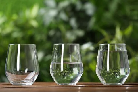 Empty, half and full glasses of water on wooden table against blurred backgro Stock Photos