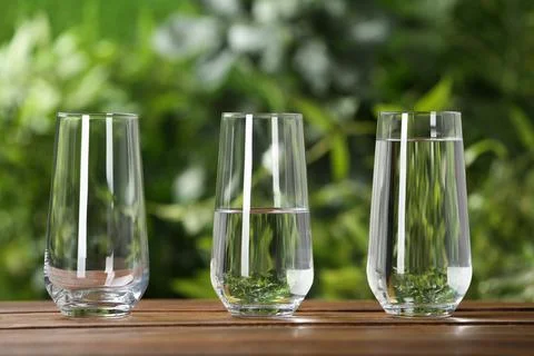 Empty, half and full glasses of water on wooden table against blurred backgro Stock Photos