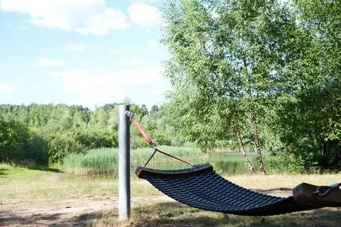 Empty hammock beside a pond in a sunny green park landscape Stock Photos