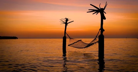 Empty hammock swinging over calm, tropical waters during sunset time Video stock 106804265