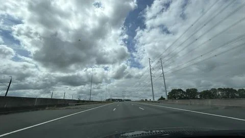 Empty highway beneath dramatic cloudy sky with power lines stretching above Stock Photos