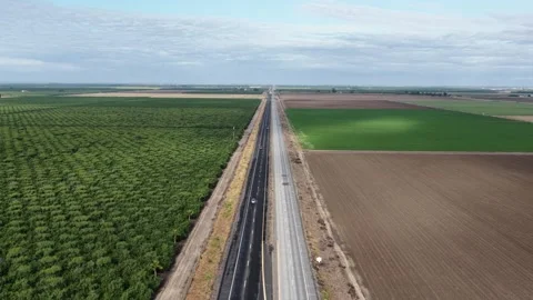 Empty highway cuts straight through patchwork farmland, lush green crop rows 動画素材 337693640