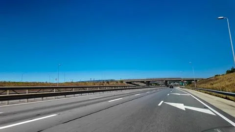 Empty highway interchange under clear blue sky with overpass, lane arrows, a Stock Photos
