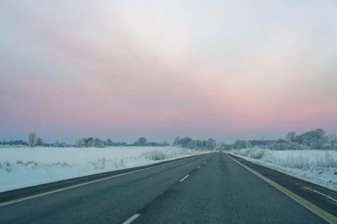 Empty highway road stretching through snowy winter landscape under pastel sky Stock Photos