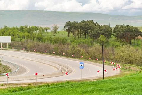 An empty highway with a sharp turn through green forest and hills Stock Photos