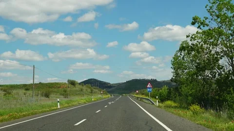 Empty highway stretching through rolling green hills under a partly cloudy sky Stock Footage 310369641