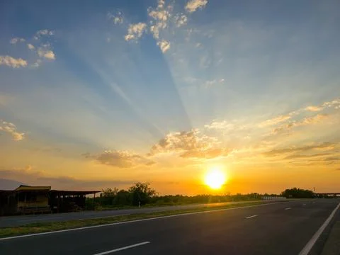 Empty highway at sunset, sun casting dramatic rays across sky and road Stock Photos