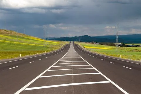 Empty Highway Through Green Fields Under Stormy Sky Stock Photos