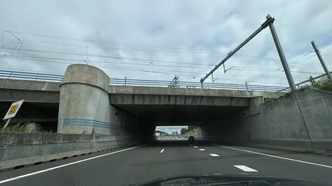 Empty highway under concrete railway overpass with overhead electric lines Stock Photos