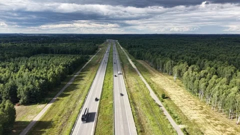 Empty highway winds through dense forest under cloudy sky Video stock 348195561