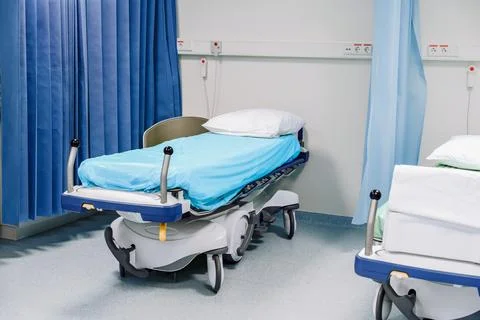 Empty Hospital Bed, Separating Blue Curtains In Ward Foto stock