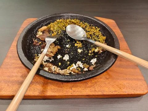 Empty hot stone plate with leftover fried rice and meat scraps after eating. Stock Photos