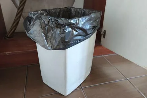 Empty household trash bin lined with a black garbage bag, placed indoors Stock-Fotos