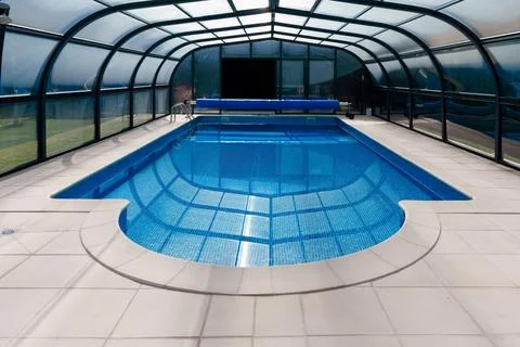Empty indoor swimming pool inside a transparent covered enclosure Stock Photos