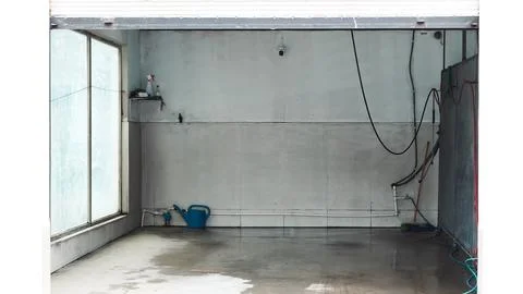 An empty industrial garage space featuring concrete walls, utility hoses, and Stock Photos