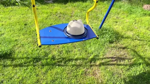 An empty iron swing is swinging with a hat on the seat. Stock Footage 211322539