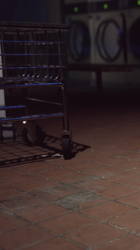 Empty laundry cart sits near a wall in a quiet laundromat at night Stock Footage 338348624