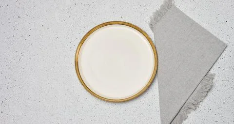 Empty light plate with golden edging next to grey linen napkin on mottled l.. Stock Photos