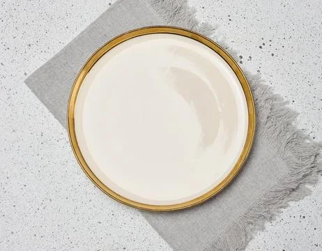 Empty light plate with golden edging next to grey linen napkin on mottled l.. Stock Photos