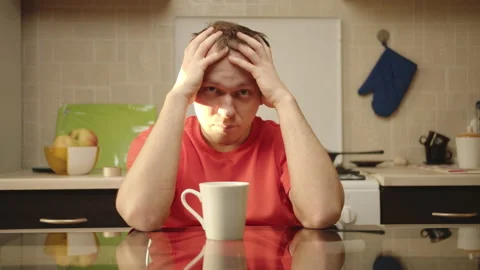 Empty look of a tired man sitting in the kitchen at the table, bright sunny day Stock Footage 130750765
