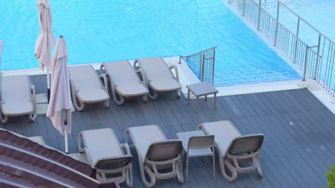 Empty lounge chairs and tables by a blue pool in 4k slow motion 60fps Stock Footage 283828659