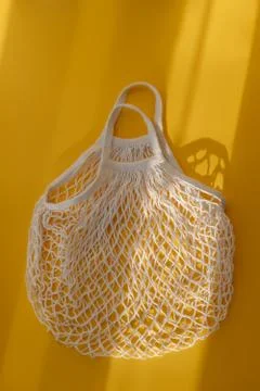 Empty mesh string bag on bright yellow background and hard sunshine. The concept Stock Photos