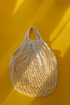 Empty mesh string bag on bright yellow background and hard sunshine. The concept Stock Photos
