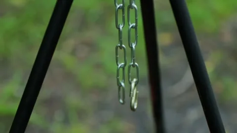 Empty metal chain hanging from black tripod, ready for campfire cooking pot, Stock Footage 339865698