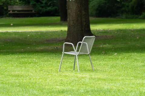 Empty metal mesh chair standing alone on grass under tree Stock Photos