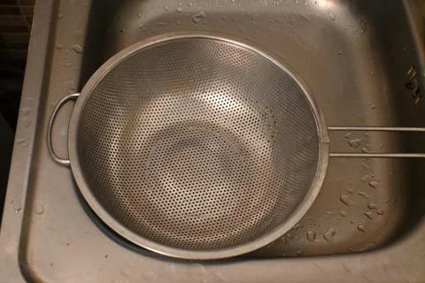 Empty metal pasta strainer in a kitchen sink Stock Photos