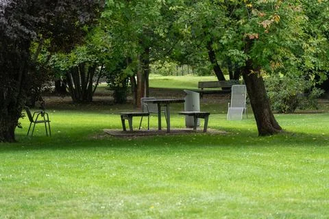Empty metal picnic table and chairs shaded by park trees Stock Photos