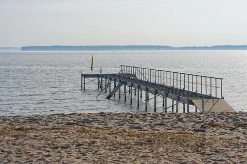 Empty metal pier extending over calm sea water on a sandy beach under clear s Stock Photos