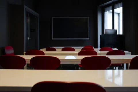 Empty modern classroom with red chairs and white desks facing blackboard Stock Photos