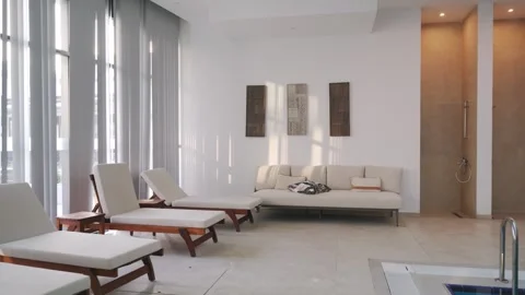 Empty modern indoor pool lounge with sunbeds. Luxury leisure area, large windows Stock Footage 270422058