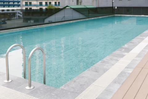 Empty modern swimming pool with clear blue water and metal ladder photograp.. Stock Photos