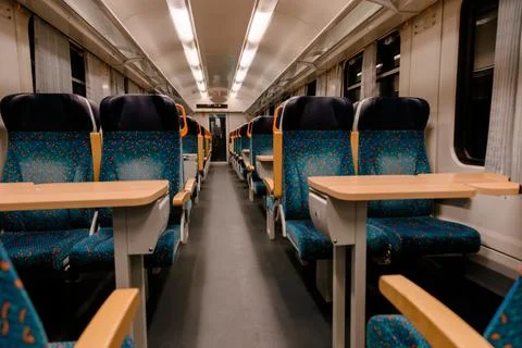 Empty modern train interior with blue seats and tables under bright lighting, Foto stock