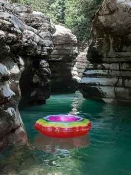 An empty multicolored swimming circle floats in the turquoise water of a canyon Stock Photos