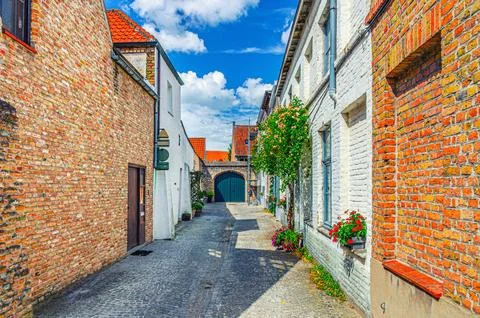 Empty narrow cobblestone dead end quiet street, buildings with flowers on bri Stock Photos