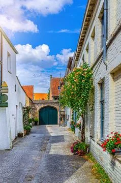 Empty narrow cobblestone dead end quiet street, buildings with flowers on bri Fotos de archivo
