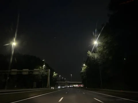 Empty night highway under glowing streetlights, dark sky, trees along roadside Stock Photos