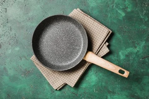 Empty non-stick frying pan with wooden handle on plaid kitchen towel and gree Photos