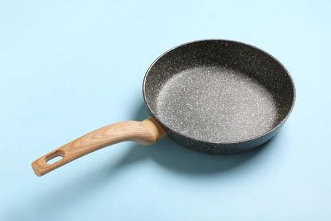 Empty non-stick frying pan with wooden handle on blue background, kitchen coo Stock Photos