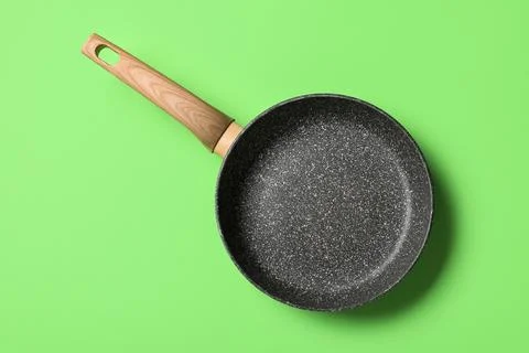 Empty non-stick frying pan with wooden handle on green background, kitchen co Stock Photos