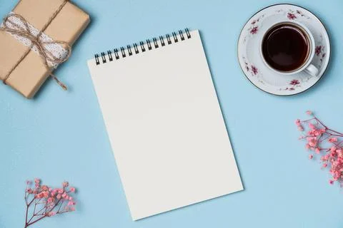 Empty notebook with gift box, cup of coffee and flowers on blue background fr Stock Photos