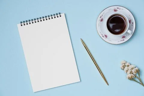 Empty notebook with gold pen, cup of coffee and flower on blue background fro Stock Photos
