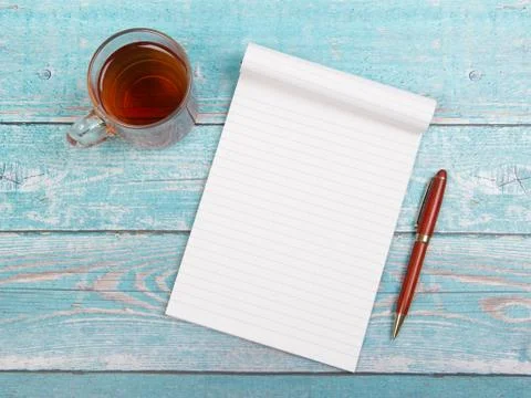 Empty notebook paper with a cup of thee and a pen on a blue wooden table Stock Photos